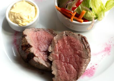 White ceramic plate with two pieces of steak, butter and salad sides
